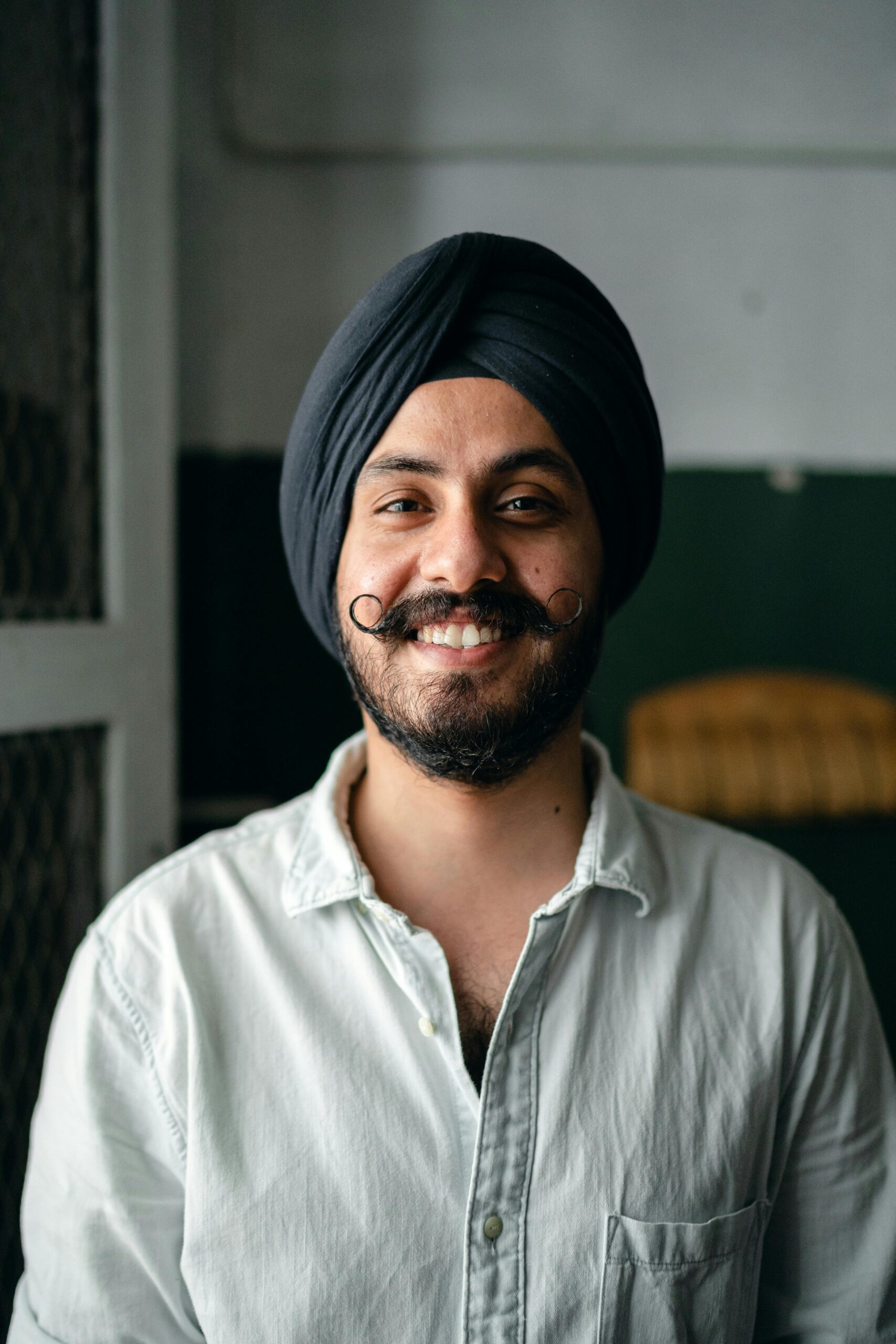 pexels photo 4307884 4307884 Positive bearded Indian male in shirt and turban standing in room and smiling while looking at camera